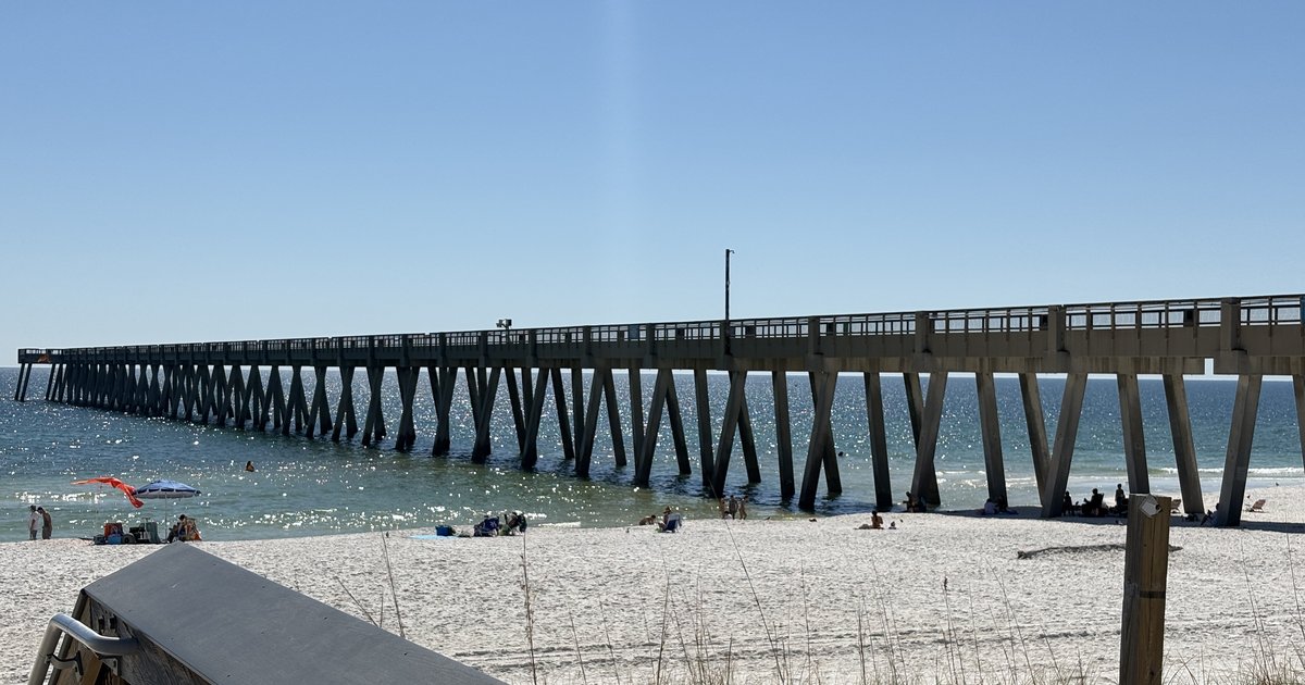 Fishing pier stretching over turquoise Gulf water from a white sand beach